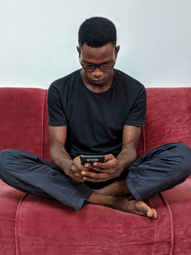 man-sitting-on-red-suede-sofa-holding-black-android-2364447.jpg